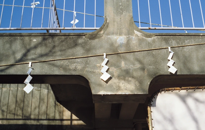 Paper gohei suspended from straw rope against the concrete structure