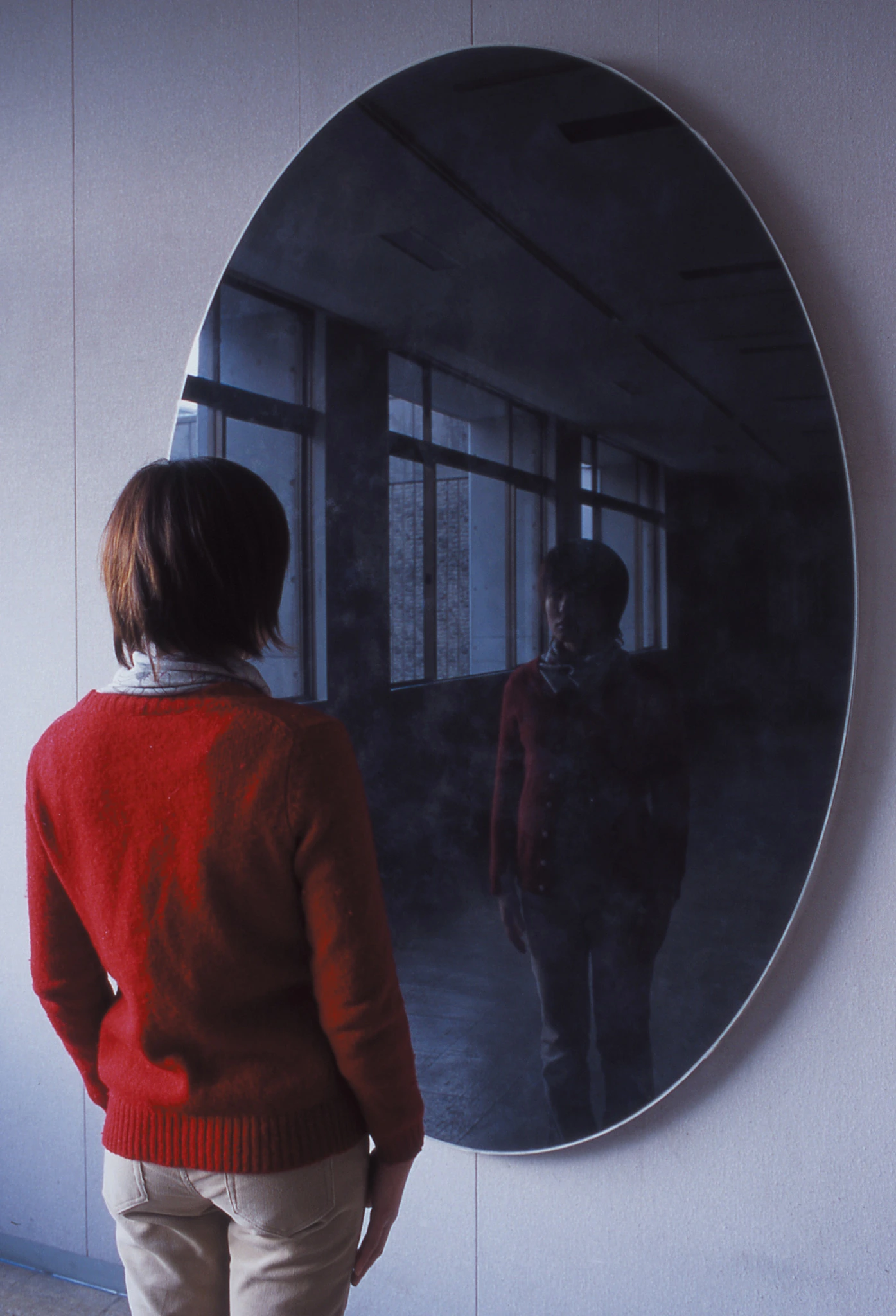 Installation view of Kuu, 2003, with a viewer standing before a large dark elliptical reflective surface