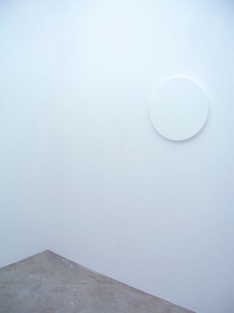 Circular white reflective surface nearly merging with the surrounding wall